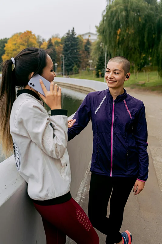 two women dressed in jogging outfits talking to each other in a park.